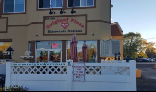 Exterior of Original Pizza restaurant with a sign, outdoor seating, and a parking area for to-go orders.