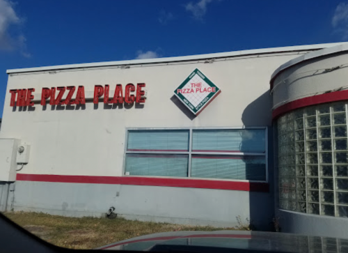 A building with a sign reading "The Pizza Place," featuring a glass block wall and a red stripe.