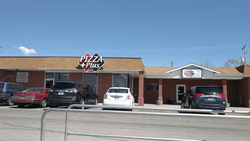 Exterior view of Pizza Plus restaurant with parked cars in front under a clear blue sky.