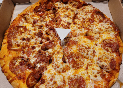 A pizza with pepperoni and cheese, partially sliced, in a pizza box with a white pizza saver in the center.