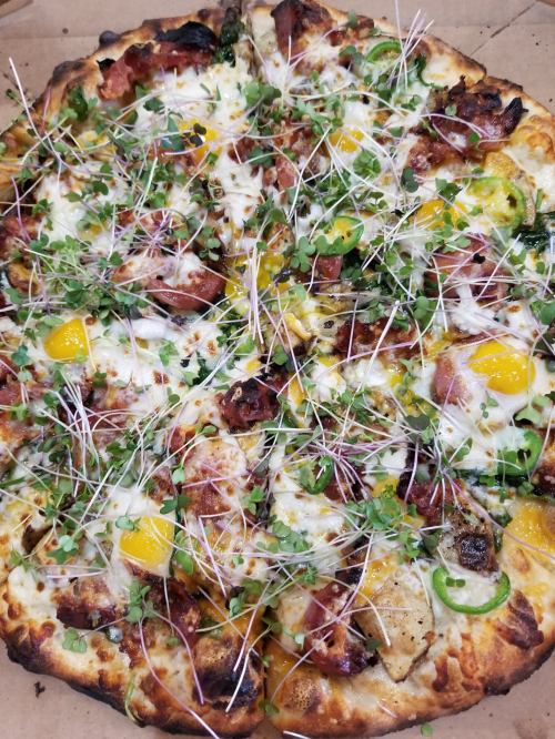 A freshly baked pizza topped with cheese, green onions, yellow tomatoes, and microgreens on a golden crust.