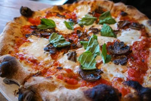 A freshly baked pizza topped with mozzarella, mushrooms, and fresh basil on a rustic wooden table.