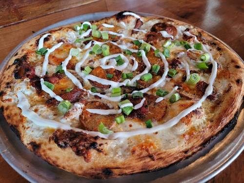 A freshly baked pizza topped with bacon, green onions, and a swirl of white sauce on a golden crust.