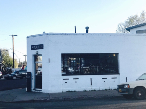 A white building with large windows, featuring a sign that reads "Pizetta," located on a street corner.