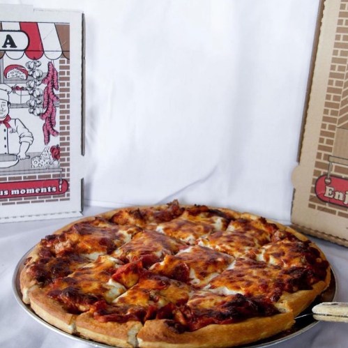 A freshly baked pizza on a silver platter, with pizza boxes in the background.