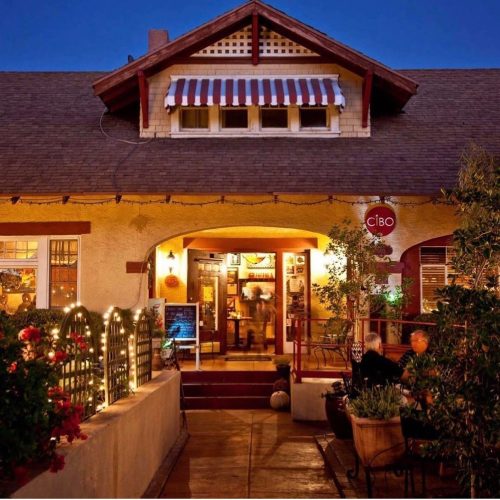 A charming restaurant entrance with a striped awning, warm lighting, and lush greenery, inviting guests inside.