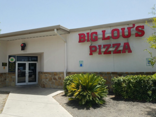 Exterior of Big Lou's Pizza, featuring a sign and entrance surrounded by greenery on a sunny day.