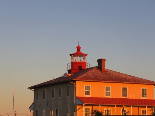 A red-roofed lighthouse atop a yellow building, illuminated by the warm glow of sunset.