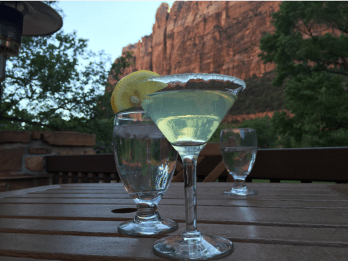 A refreshing cocktail with a lemon slice and salt rim, alongside a glass of water, set against a scenic mountain backdrop.