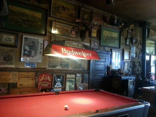 A cozy bar interior featuring a pool table, Budweiser sign, and vintage decor on the walls.