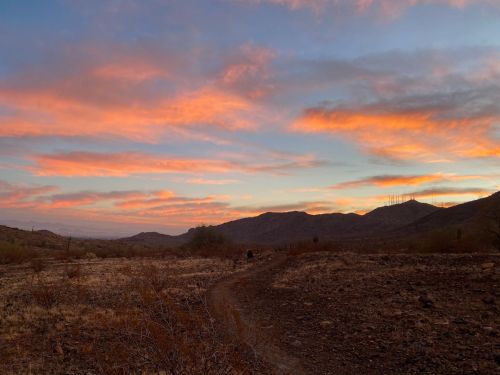 A scenic view of a desert landscape at sunset, with colorful clouds and distant mountains under a vibrant sky.