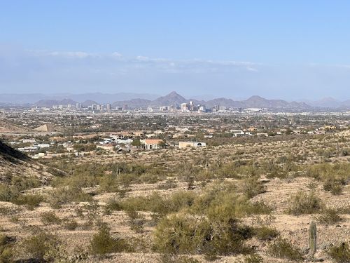 A panoramic view of a desert landscape with distant mountains and a city skyline under a clear blue sky.