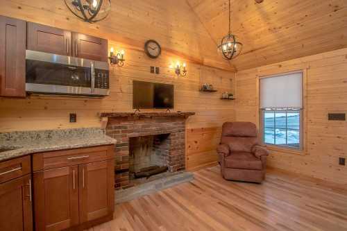 Cozy wooden interior with a kitchen area, fireplace, TV, and a recliner chair, featuring warm lighting and hardwood floors.