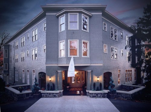 A gray, multi-story building with a welcoming entrance and decorative landscaping, set against a twilight sky.
