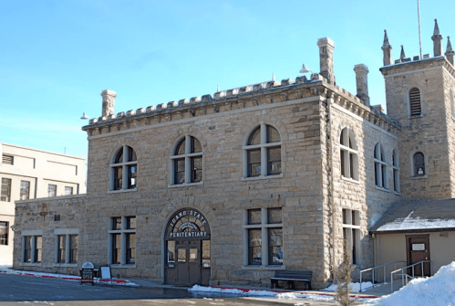 Historic stone building of the old state penitentiary, featuring arched windows and a tower, surrounded by snow.