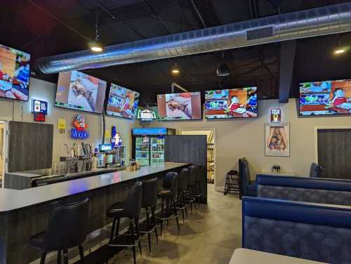 A modern bar area with multiple TVs showing sports, featuring a sleek counter and blue seating.