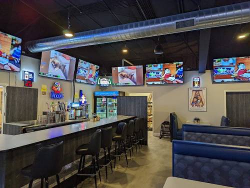 A modern bar area with multiple TVs showing sports, featuring a sleek counter and blue seating.