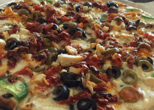 A close-up of a pizza topped with olives, green peppers, chicken, and various cheeses.