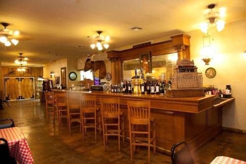 A rustic restaurant interior featuring a wooden bar, high stools, and vintage decor with warm lighting.