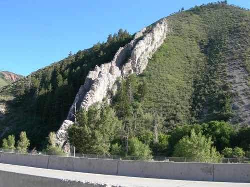 A rocky hillside with steep white cliffs and green vegetation under a clear blue sky.