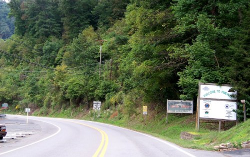 A winding road leads into a wooded area with welcome signs for a county and nearby attractions.