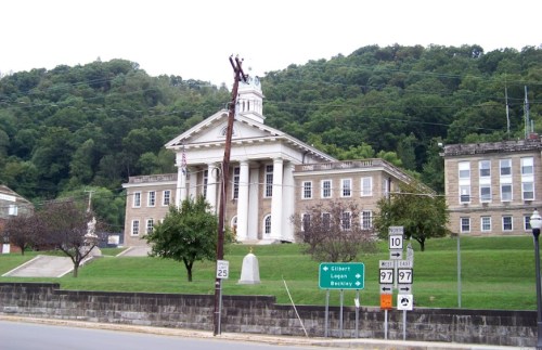 Historic building with columns, surrounded by trees and signage for nearby towns, set against a hilly backdrop.