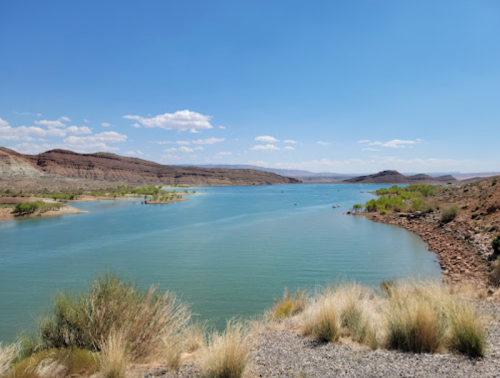 A serene lake surrounded by rocky hills and sparse vegetation under a clear blue sky.