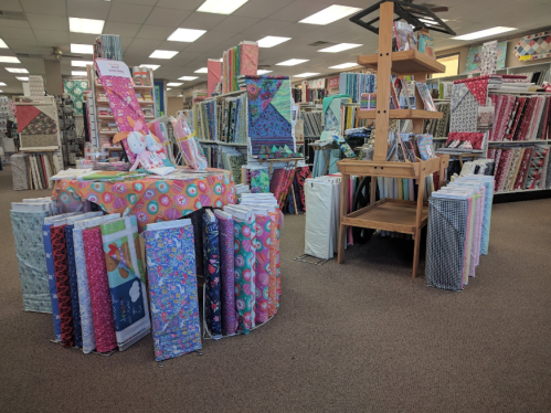 A fabric store interior filled with colorful rolls of fabric arranged on shelves and tables.