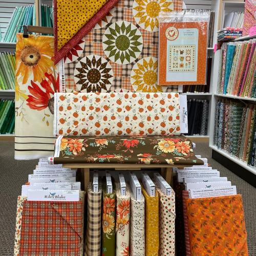 A display of colorful fabric patterns, including floral and autumn designs, arranged on shelves in a craft store.