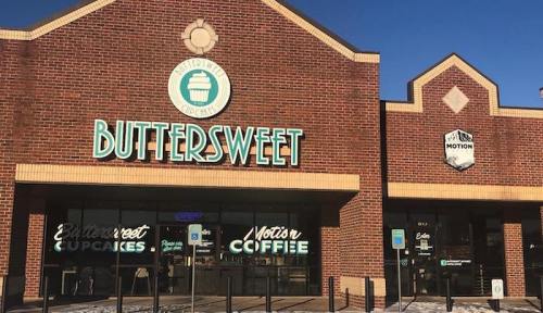 Exterior of a brick building featuring "Buttersweet Cupcakes" and "Motor's Coffee" signs. Clear blue sky above.