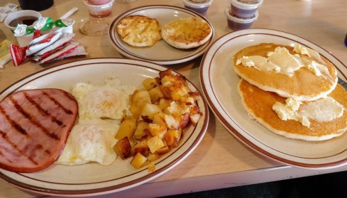 A breakfast spread featuring eggs, ham, hash browns, a toasted English muffin, and pancakes with butter.