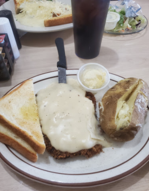 A plate with fried chicken smothered in gravy, a baked potato with butter, and two slices of toast.