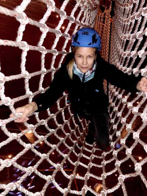 A person in a blue helmet climbs through a rope net, showcasing an adventurous indoor activity.