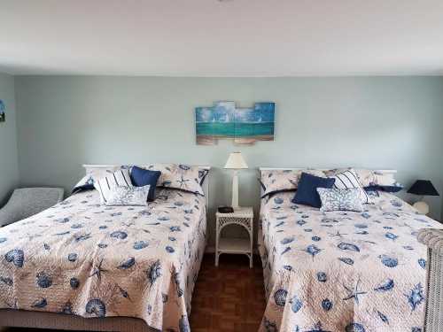 A cozy room with two beds, light blue walls, and beach-themed decor, featuring seashell-patterned quilts and pillows.