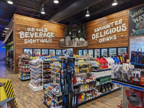 A store interior featuring shelves of drinks and snacks, with a wooden wall displaying "Ice Cold Beverage Sighting!" and "Encounter Delicious Drinks."