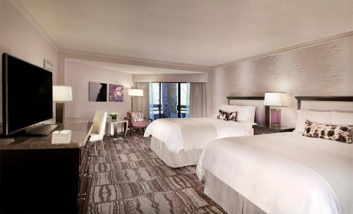 A modern hotel room featuring two beds, a large TV, and a seating area with natural light from a window.