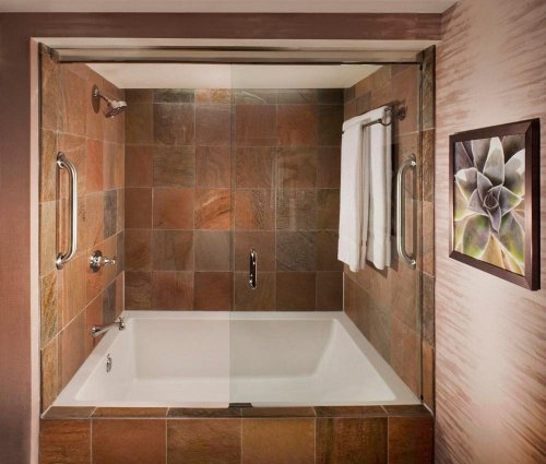 A modern bathroom featuring a glass-enclosed bathtub with stone tiles and a decorative wall art piece.