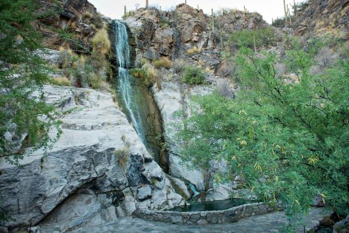 A serene waterfall cascading down rocky cliffs, surrounded by lush greenery and a small pool at the base.