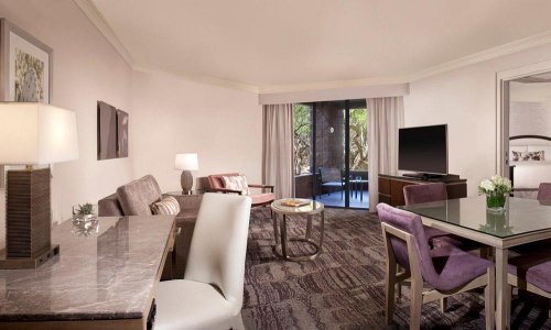 A spacious hotel suite featuring a living area, dining table, and balcony with outdoor seating. Modern decor throughout.