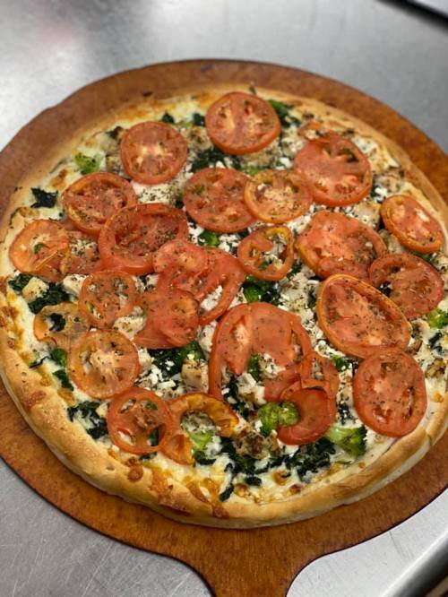 A freshly baked pizza topped with sliced tomatoes, spinach, and cheese on a wooden pizza board.