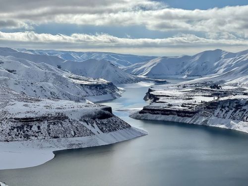 A serene winter landscape featuring snow-covered mountains and a winding river reflecting the sky.