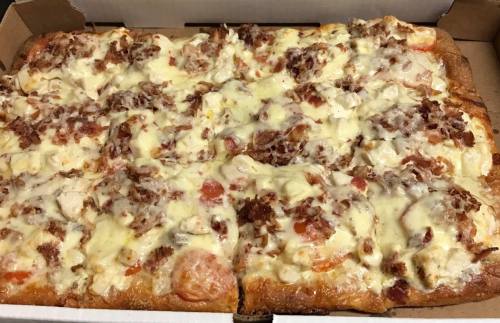 A rectangular pizza topped with melted cheese, bacon, and tomatoes in a cardboard box.