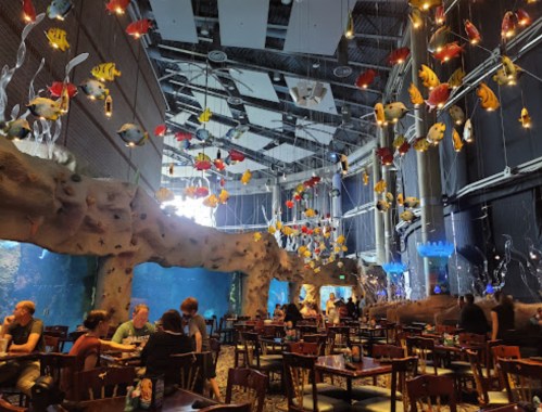 A vibrant restaurant interior with colorful fish decorations and an aquarium, featuring tables and diners.