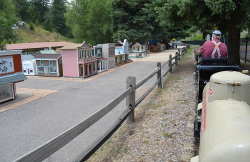 A miniature town with colorful buildings along a path, viewed from a train track with a train in the foreground.