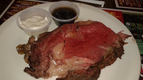 A plate of prime rib served with two dipping sauces, one dark and one creamy, on a restaurant table.