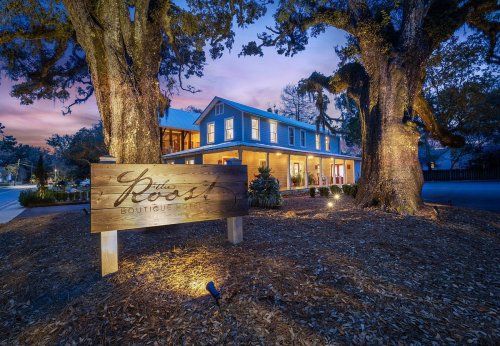 A boutique building at dusk, surrounded by large trees and illuminated by soft lights, with a welcoming sign in front.