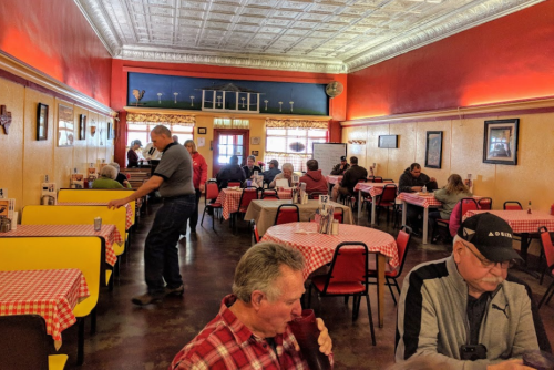 A colorful diner with checkered tablecloths, patrons dining, and a server attending to tables in a lively atmosphere.
