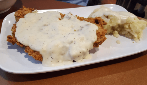 A plate of fried chicken smothered in creamy gravy, served with a side of mashed potatoes.
