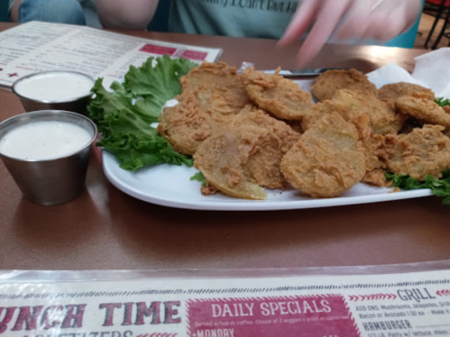 A plate of crispy fried pickles served with ranch dressing on the side, garnished with lettuce.