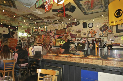 A cozy restaurant interior filled with eclectic decor, lights, and a counter displaying various pies.